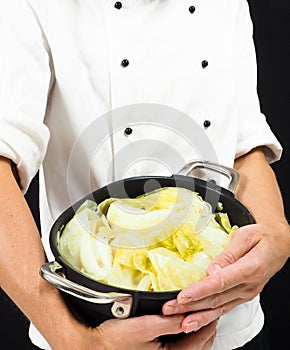 Chef in white jacket holding around a casserole