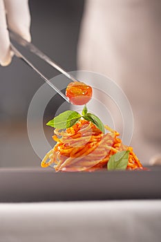 A chef in a white uniform and gloves serves cherry tomatoes in pasta in tomato sauce with tweezers