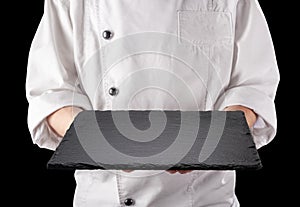 Chef in white uniform is holding an empty black slate serving plate. Black background