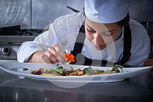 Chef woman garnishing flower in dish at kitchen photo