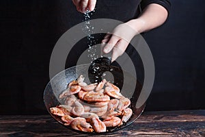 Chef at work. Hand holds a hot pan with fried shrimp and salt the food