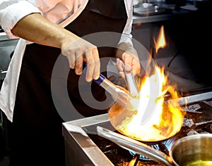 Chef cooking with flame in a frying pan on a kitchen stove