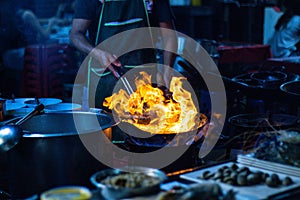 The chefs are cooking with fire over the pan, at street food dining options in all of Bangkok, Yaowarat road or Chinatown Thailand