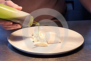 Chefs hand pouring sauce from a bottle onto a fish dish photo