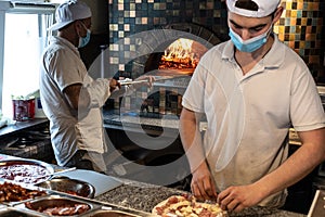 Chefs preparing pizza in a pizzeria wearing masks and protections during covid or coronavirus emergency