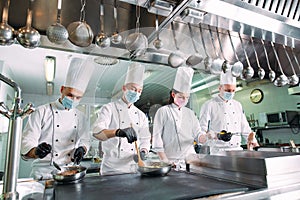 Chefs in protective masks and gloves prepare food in the kitchen of a restaurant or hotel.