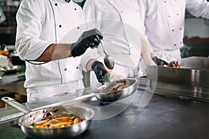 Chefs in protective masks and gloves prepare food in the kitchen of a restaurant or hotel.