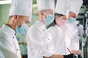 Chefs in protective masks and gloves prepare food in the kitchen of a restaurant or hotel.