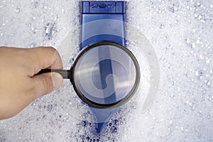 Chemical components on the shampoo label: Sodium Lauryl Sulfate sls, sles. A hand holds a blue jar and a magnifier, where the photo