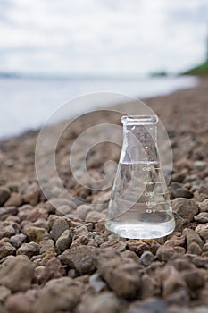 Chemical flask with water, lake or river in the background.