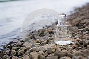 Chemical flask with water, lake or river in the background.