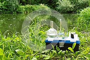 Chemical flasks and chemicals in glass bottles against the background of a natural reservoir. Water sampling