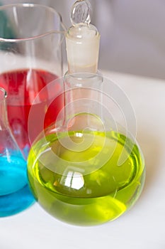 Chemical flasks with colored chemicals in tubes and flasks. Round capacity with green beverage inside. Selective focus, vertical