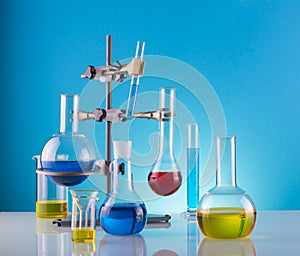 Chemical flasks with multi-colored reagents and a rack close-up on a blue