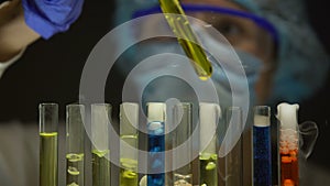 Chemist checking sediment in tube with yellow liquid, substances emitting smoke