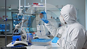 Chemist with coverall analysing bacteria sample from petri dish