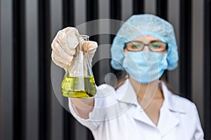 Chemist examining test tube with substance. She`s in protective uniform over grey abstract grey background