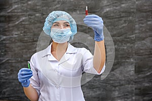 Chemist examining test tube with substance. She`s in protective uniform over grey abstract grey background