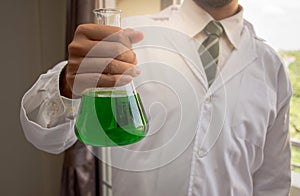 Chemist is holding the glass conical flask with a green liquid chemical solution