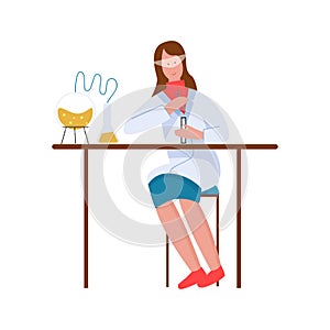 Chemist holding test tube for chemical experiment in laboratory, woman in safety glasses sitting at table