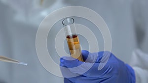 Chemist in protective uniform taking toxic liquid sample from test-tube, danger