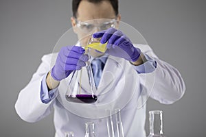 Chemist researcher in blue gloves and glasses pouring colorful liquids in flask