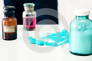 Chemistry bottles containing various substances of different colors standing on laboratory table seen along a pile of blue powder