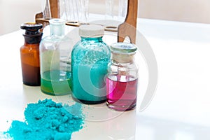 Chemistry bottles containing various substances of different colors standing on laboratory table seen over a pile of blue powder