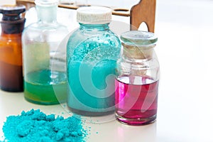 Chemistry bottles containing various substances of different colors standing on laboratory table seen over a pile of blue powder