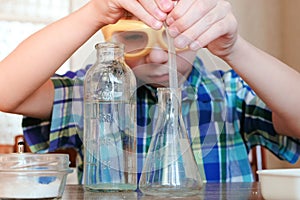 Chemistry experiments at home. Boy pours water from the bottle into the flask using a pipette.
