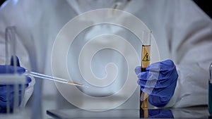 Chemistry lab worker studying sample of detergent from tube with caution sign