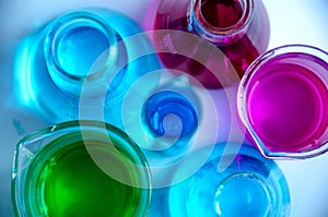 Chemistry laboratory glassware containing pink , blue and green solutions on a reflecting surface and periodic table background