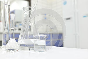 Chemistry Science laboratory flask, beaker and glassware with clear liquid chemical in blur background.