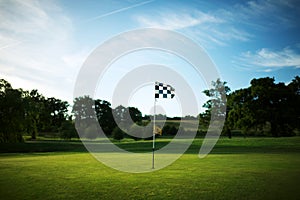 Chequered flag on a golf course green with a blue sky