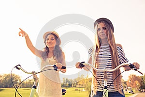 Cherful happy girls with hat ride bicycles and pointing away photo