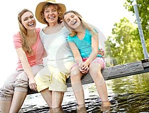 Cherishing the good times. A cute young girl sitting on a pier at the lake with her mother and granny.