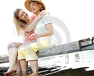 Cherishing the time together. A mature woman embracing her mother while sitting on a jetty by the lake.