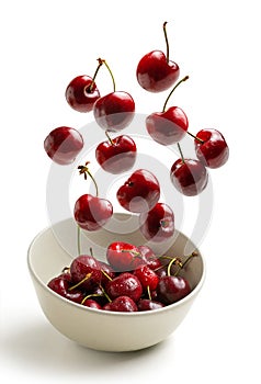 Cherries flying in white bowl isolated from background