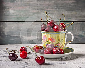 Cherries in a mug with a picture on a saucer on a table