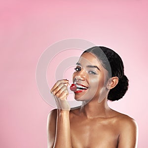 Cherries are my happy drugs. a beautiful young woman eating a cherry against a pink background.