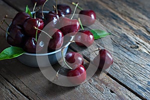 Cherries are placed in the zinc cup and put on a rustic wooden floor, horizontal closeup.