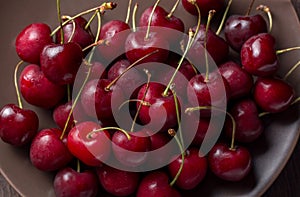 Cherries on a plate, on a wooden background. Summer picnic, harvest, treats. Food for vegetarians and vegans.