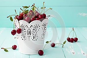 Cherries in a small white bucket on old vintage wooden background.