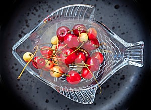 Cherries of varying degrees of greenness in a decorative glass vase on a dark background close-up photo