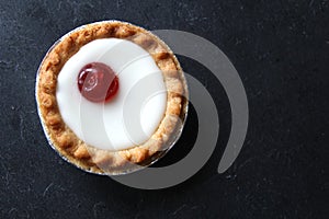 Cherry bakewell tart in foil case on dark background