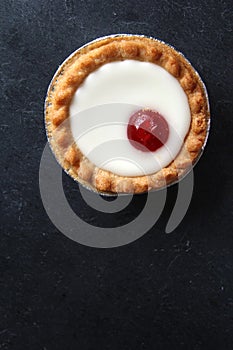 Cherry bakewell tart in foil case on dark background