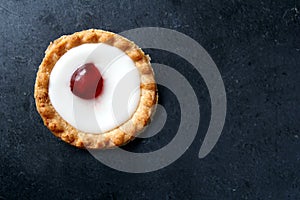 Cherry bakewell tart in foil case on dark background