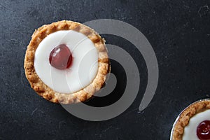 Cherry bakewell tarts in foil cases on dark background