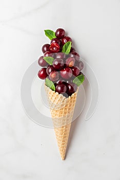 Cherry berries with mint in waffle ice cream cone on white marble background. summer food concept. top view. flat lay