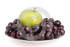 Cherry berries and one big green apple on white plate white background isolated close up macro
